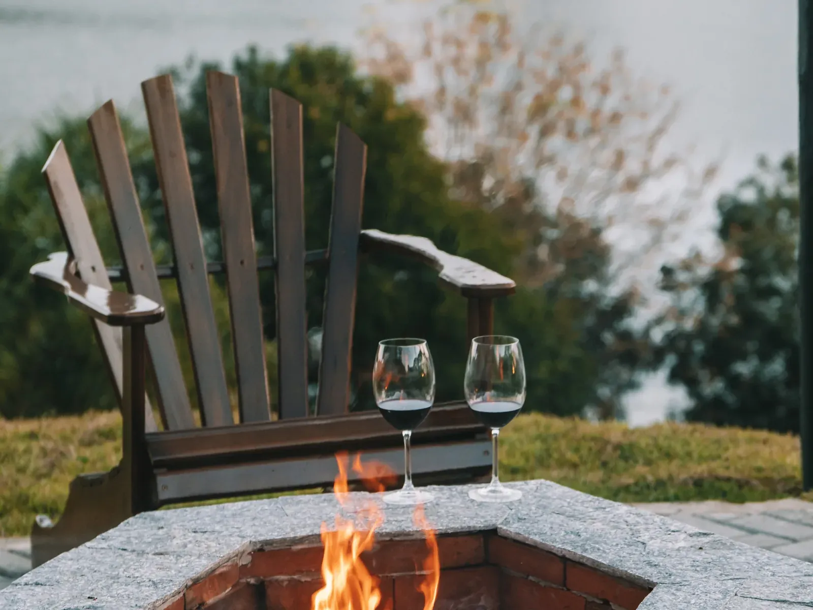Fogo de chão com cadeira de madeira e duas taças, com o lago ao fundo